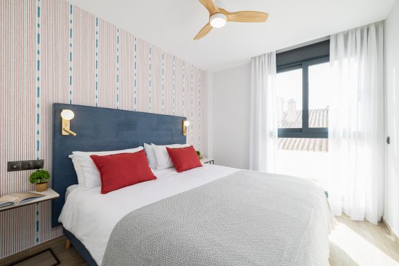 Habitación luminosa con cama doble, paredes de diseño y ventanas amplias.